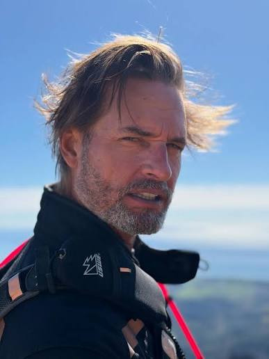 Original outdoor three-quarter portrait of Daniel, an editorial alias, with windswept hair and a salt-and-pepper beard.