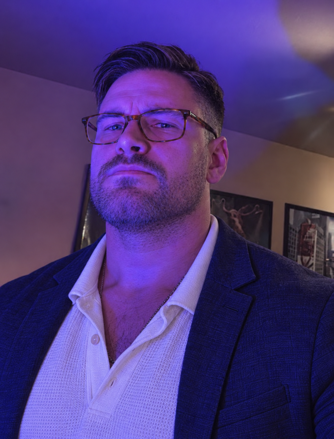 AI style preview of Max with side-swept hair, tapered sides, short stubble, rectangular tortoiseshell glasses, a cream polo and navy jacket.