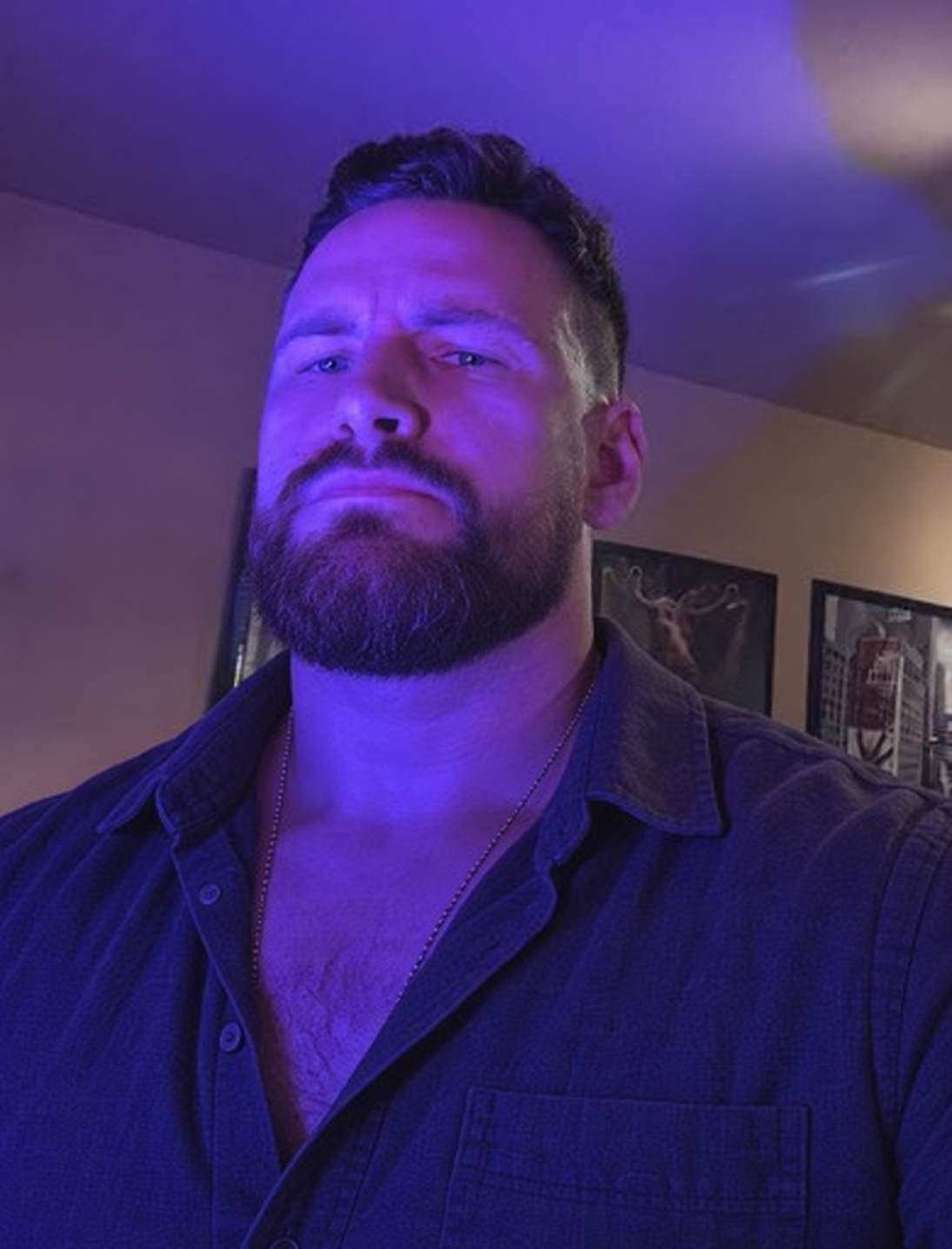 AI styling concept under purple light with a tidier full beard, short textured hair and a dark open-collar overshirt.