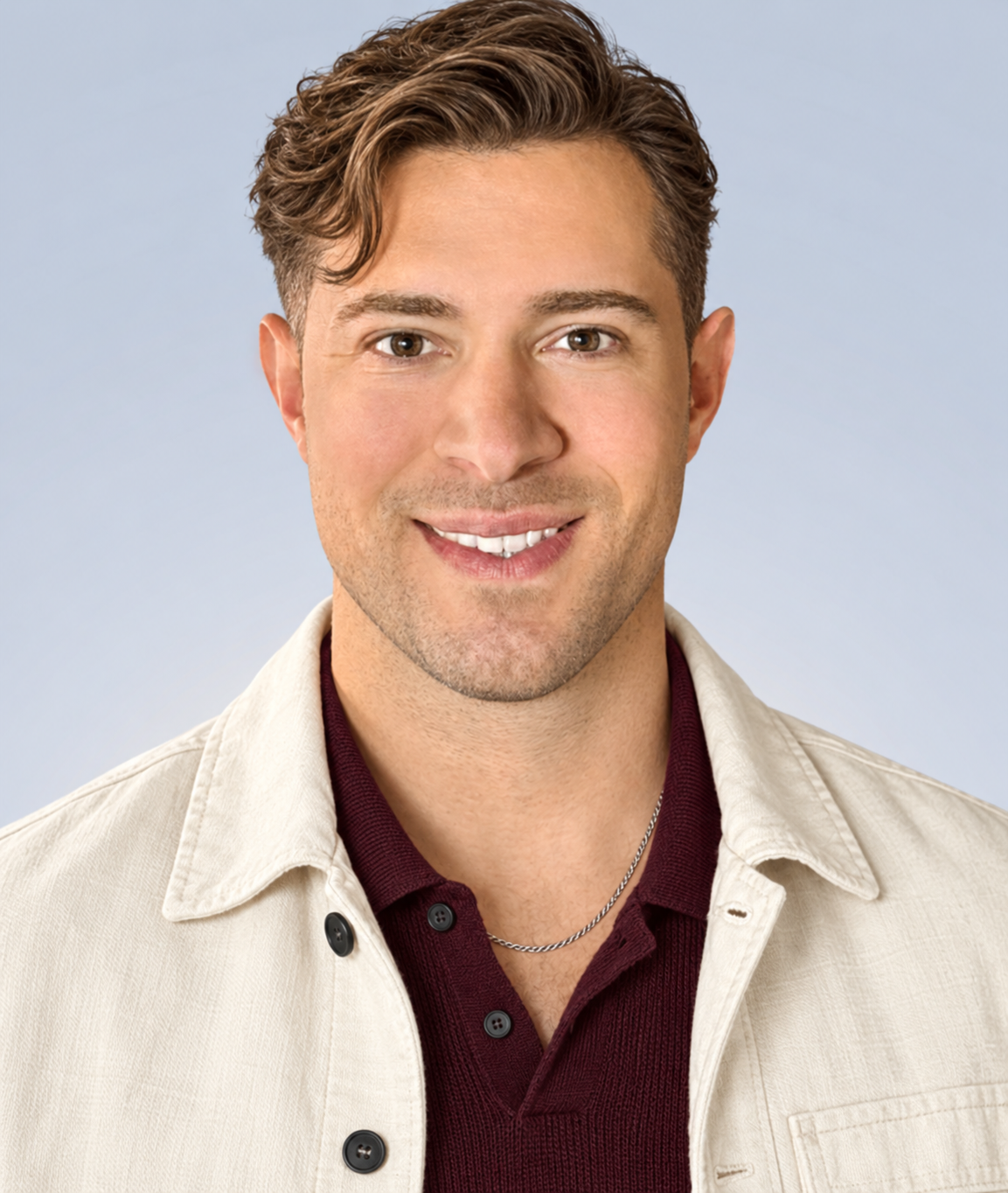 AI style preview of Oliver with side-swept wavy hair, faint stubble, an ivory chore-style jacket, burgundy knit polo and silver-toned chain.